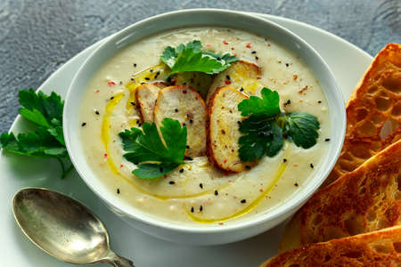 Creamy chicken soup with vegetables in bowl with chiabatta toast, parsley and nigela seeds sprinkle on stone tableの写真素材