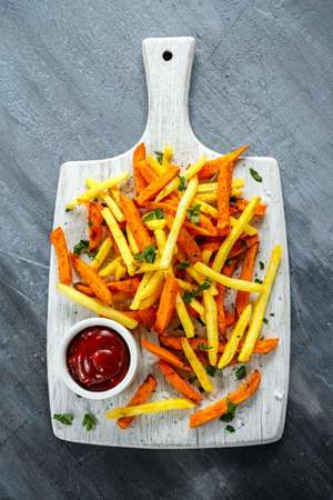 Healthy Homemade Baked Orange Sweet Potato and french Fries with ketchup, salt, pepper on white wooden boardの写真素材