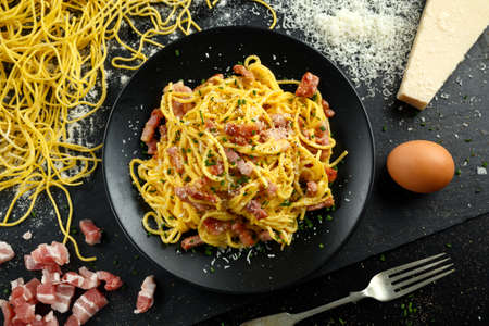 Classic Homemade Pasta carbonara Italian with Bacon, eggs, Parmesan Cheese on black plate.の写真素材
