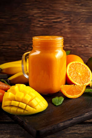 Fresh Orange smoothie drink with banana, mango, carrots on black wooden boardの写真素材
