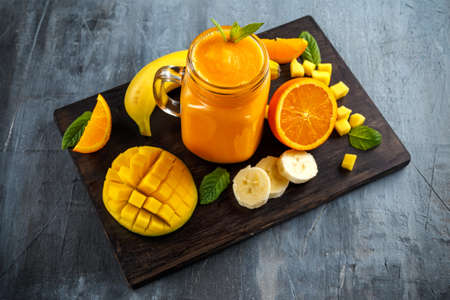 Fresh Orange smoothie drink with banana, mango on black wooden boardの写真素材