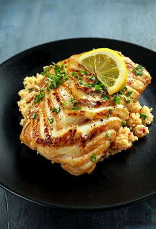 Soy-glazed cod loin fillet with cous-cous salad on black plateの写真素材