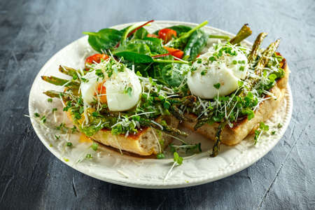 Healthy Breakfast Smashed Avocado, asparagus and poached egg on grilled toasts for breakfast served with salad and plum tomatoesの写真素材