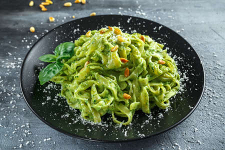 Tagliatelle pasta with pesto sauce, pine nuts and parmesan on black plate.
