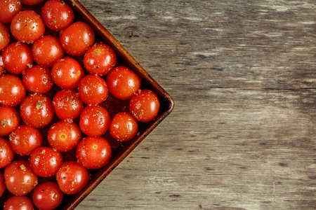 Cherry tomatoes with salt, pepper and olive oil in vintage baking tray on wooden tableの写真素材
