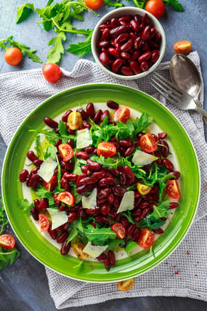 Red beans and wild rocket healthy salad with cherry tomatoes, sea salt flakes and parmesan shavings drizzled with olive oilの写真素材