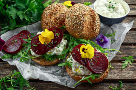 Rustic wholegrain buns with cottage cheese, rocket leaves, beetroot slices and edible viola flowers. Vegetarian food snack.の写真素材
