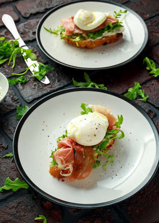 Bruschetta with cream cheese, wilde rucola, parma ham and poached egg served on white plate.の写真素材