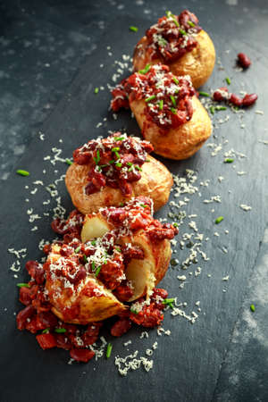 Baked jacket potatoes topped with red kedney beans in tomato sauce and chives served on stone boardの写真素材
