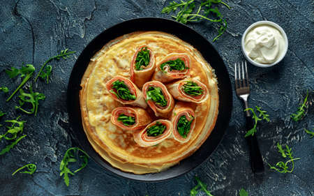Crepes pancakes rolls with smoked salmon stuffed with wild rocket salad filling served on black plate with fresh creme.の写真素材