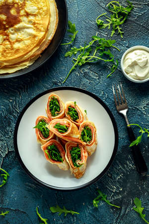 Crepes pancakes rolls with smoked salmon stuffed with wild rocket salad filling served on plate with fresh cremeの写真素材