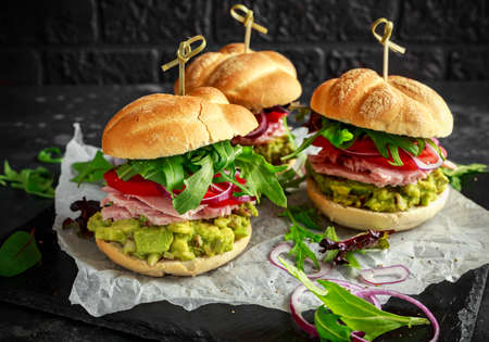 Fresh home sandwich with avocado guacamole, tomatoes, arugula, red onion and ham.の写真素材