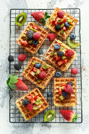 Fresh egg waffles dessert for breakfast with fruits strawberries, blueberries, blackberries, raspberries and kiwiの写真素材