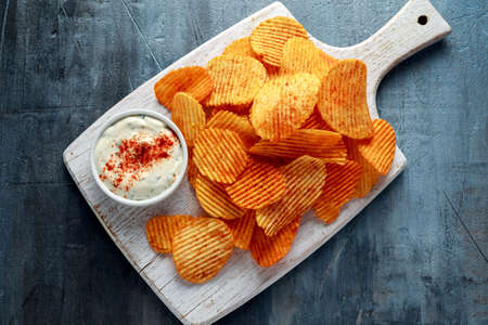 Potato chips, snack crisps with red paprika and white dip sauce on white board.の写真素材