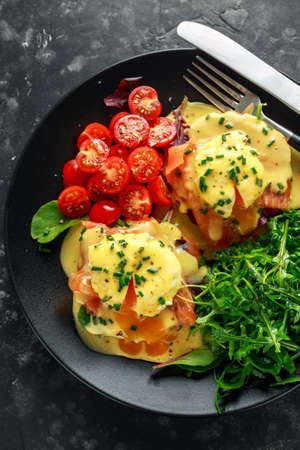 Eggs Benedict on english muffin with smoked salmon, wild rocket and hollandaise sauce in a black...