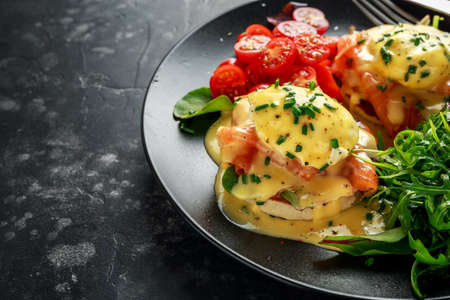 Eggs Benedict on english muffin with smoked salmon, wild rocket and hollandaise sauce in a black plate.の写真素材