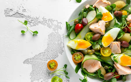 Healthy Nicoise salad with salmon, colourful sweet cherry tomatoes, olives, green beans, cucumber ribbons, soft boiled eggs, water-cress leaves with Mediterranean seasoningの写真素材