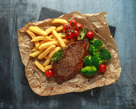 Grilled sirloin steak with potato fries, broccoli and cherry tomatoes on crumpled paperの写真素材