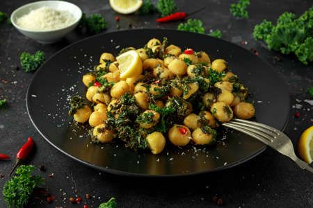 Fried kale and potato gnocci with chilie, peccorino cheese and lemon wedges in black plate. Italian...