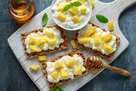 Homemade Crispbread toast with Cottage Cheese, Pineapple and honey on white wooden board.の写真素材