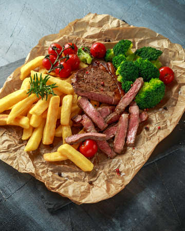Grilled sirloin steak with potato fries, broccoli and cherry tomatoes on crumpled paperの写真素材