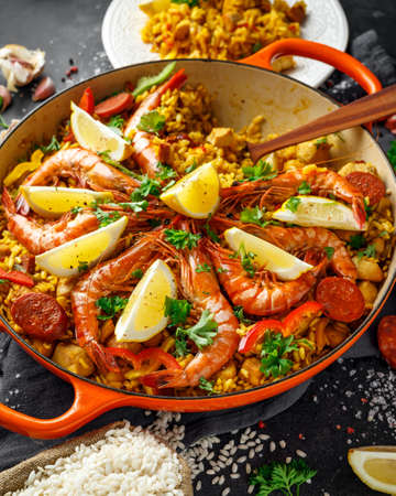 Traditional paella in the fry pan with chicken, prawns, spicy chorizo, lemon and glass of white wine.の写真素材