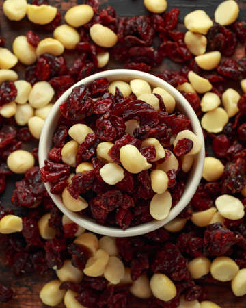 Healthy snack of Dried cranberries and macadamia nuts in a ceramic bowl on rustic wooden tableの写真素材