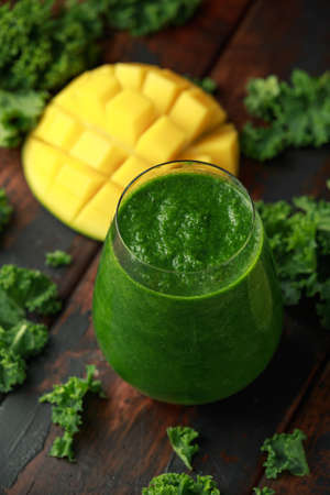 Green smoothies with kale and mango on wooden table.