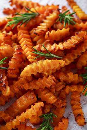 Baked butternut squash fries with sea salt and rosemary. Pumpkin chips on white wooden board.
