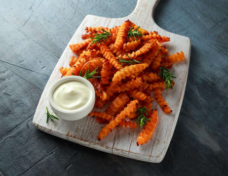 Baked butternut squash fries with sea salt and rosemary. Pumpkin chips on white wooden board.