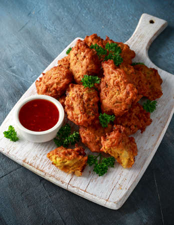Crispy onion bhajis with sweet chilli sauce on white wooden boardの写真素材