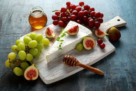 Cheese brie with figs, green and red grape and honey on white wooden boardの写真素材