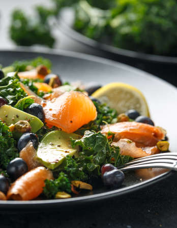Salmon Kale super food Salad with avocado, pistachio nuts and blueberries on black plate
