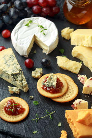Cheese platter served with grapes, ale chutney, honey, crackers on stone board. Brie, cheddar, red...