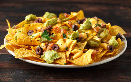 Mexican nachos tortilla chips with olives, jalapeno, guacamole, tomatoes salsa and cheese dip. close upの写真素材