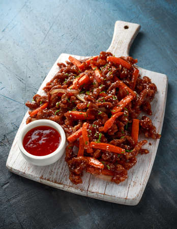 Crispy shredded beef with carrots and sweet chilli sauce on white wooden board. Chinese takeaway...