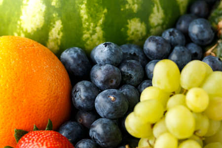 Variety of fresh fruits and berries on dark background: cantaloupe, melon, watermelon, blueberry,...