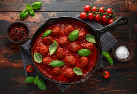 Homemade Meatballs in iron cast with sweet and hot tomato sauce, basil. On wooden table
