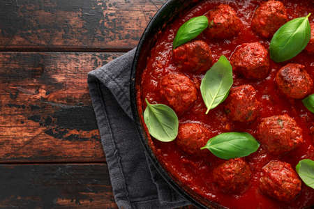 Homemade Meatballs in iron cast with sweet and hot tomato sauce, basil. On wooden tableの写真素材