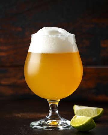 Glass of chilled unfiltered beer with lime wedges on wooden background