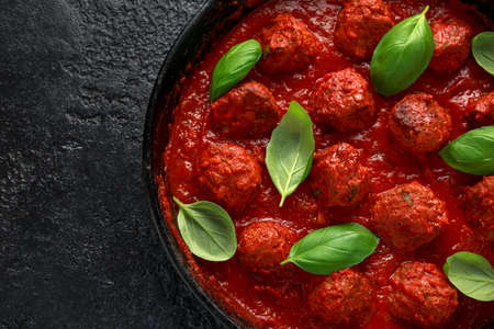 Homemade Meatballs in iron cast with sweet and hot tomato sauce, basil. On wooden table.の写真素材