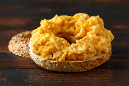 Bagels breakfast sandwich with scrambled eggs on wooden tableの写真素材