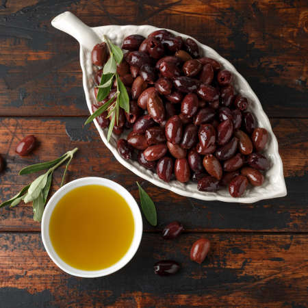 Extra virgin olive oil and kalamata olives on rustic wooden background.