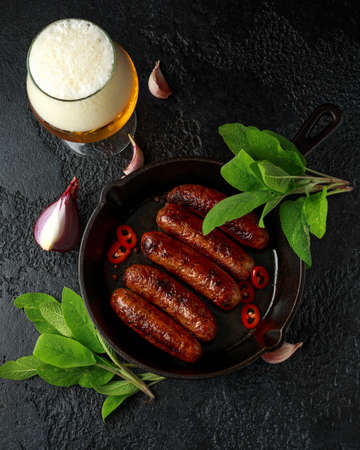 Butcher made sage and onion sausages baked in cast iron skillet, pan and glass of cold beerの写真素材