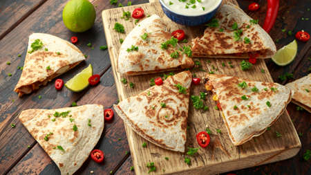 Mexican quesadilla with chicken, corn, black beans, cheese, vegetables, lime and yogurt sauce on wooden board.の写真素材