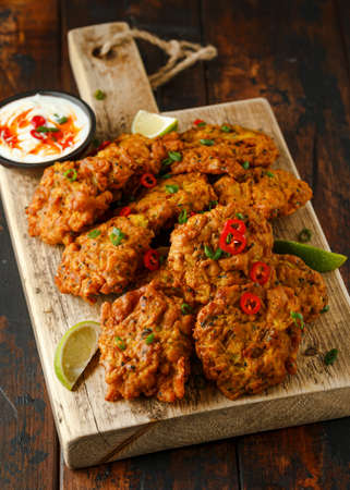 Indian takeaway food, spicy onion bhajis served with chili yoghurt dip and lime wedges on wooden...