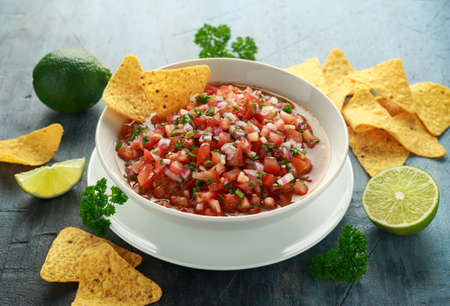 Mexican Tomato Salsa in white bowl with lime, red onion, jalapeno pepper, parsley and tortilla chipsの写真素材