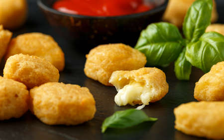 Fried mozzarella, cheddar cheese bites, balls with ketchup on rustic stone boardの写真素材