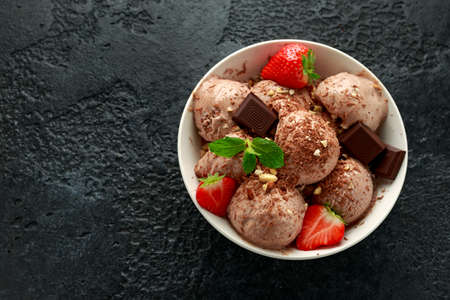 Chocolate Ice Cream with dark chocolate bars, strawberry and hazelnuts in a white bowl.