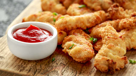 Buttermilk chicken nuggets with ketchup on wooden board.